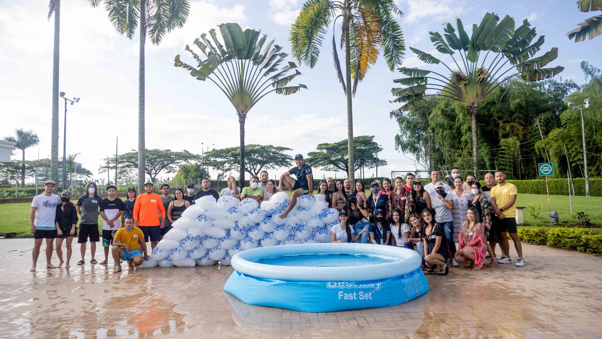 Un grupo de personas posa con una pequeña piscina inflable y montones de globos blancos en un parque.