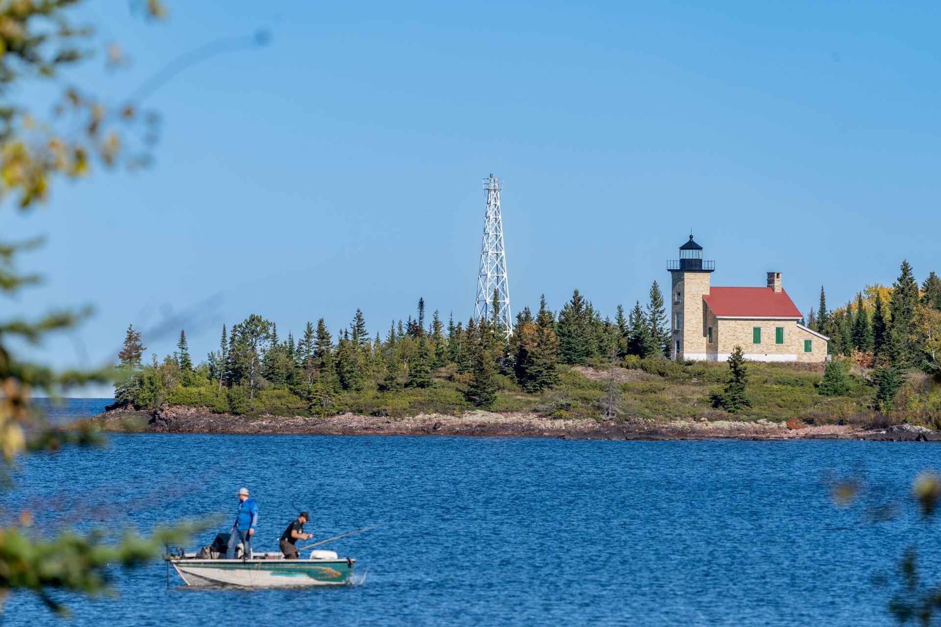 A man is fishing in a boat on a lake with a lighthouse in the background.