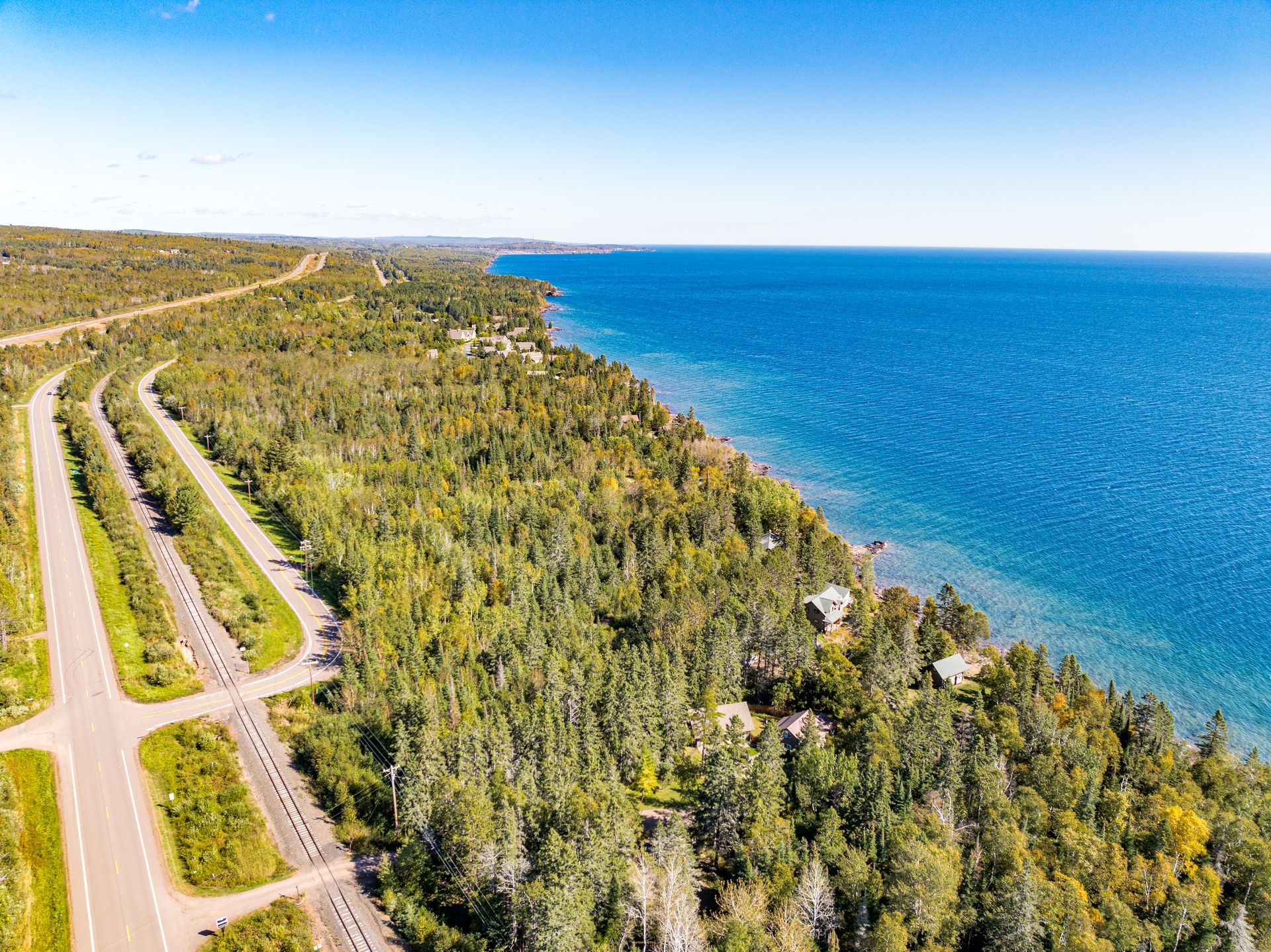 An aerial view of a road going through a forest next to a body of water.
