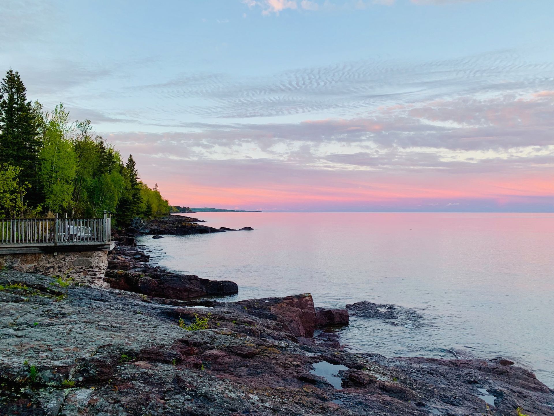 A rocky shoreline of a lake with a sunset in the background.