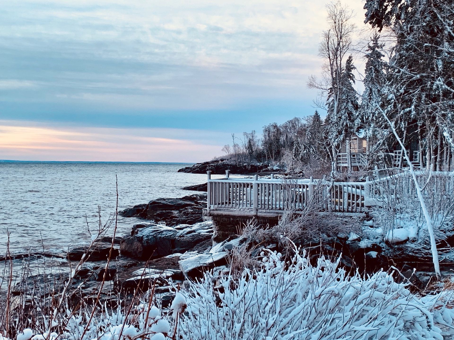 A snowy beach with a bridge over the water and trees covered in snow.