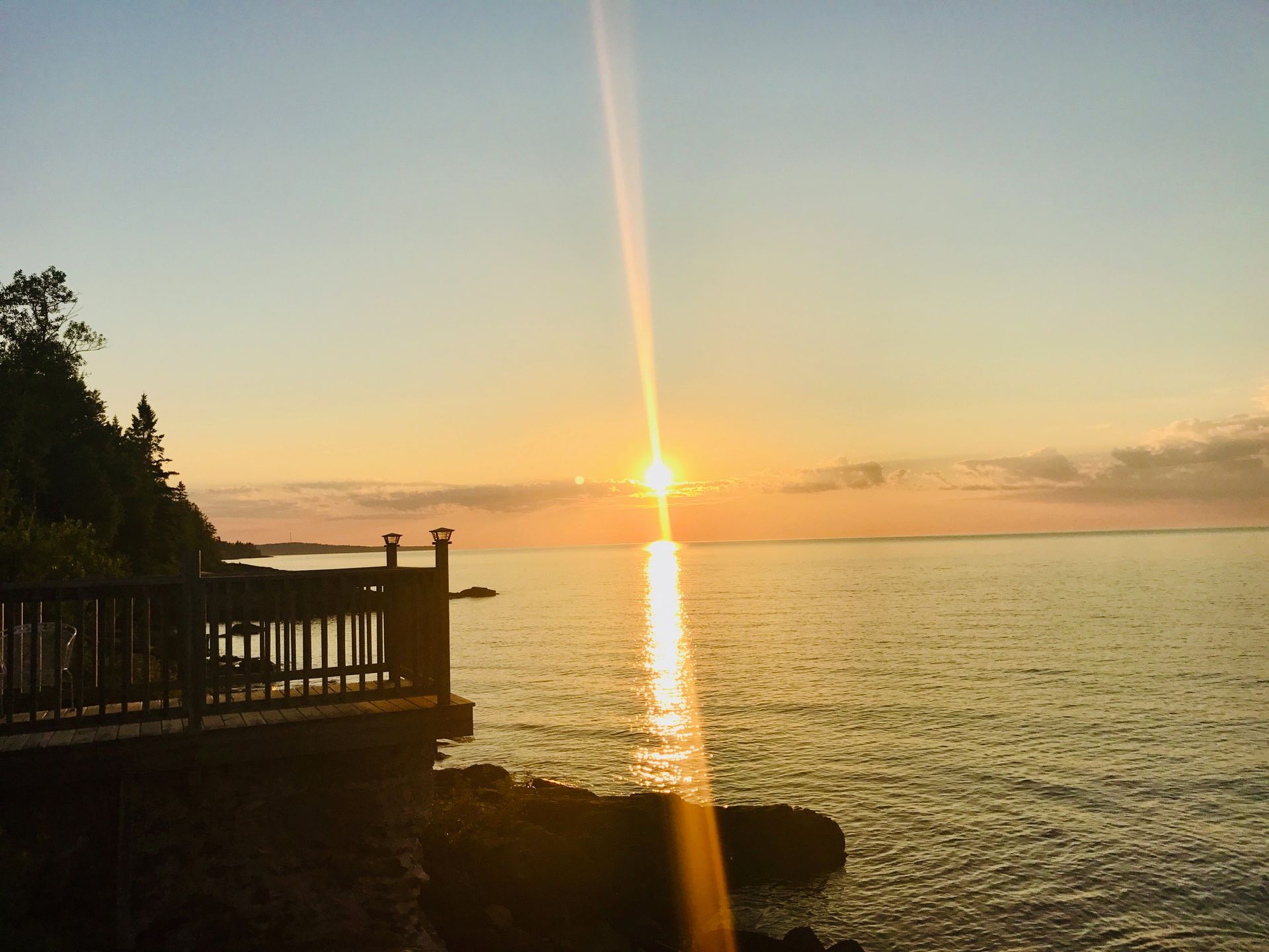 The sun is setting over the ocean with a dock in the foreground.