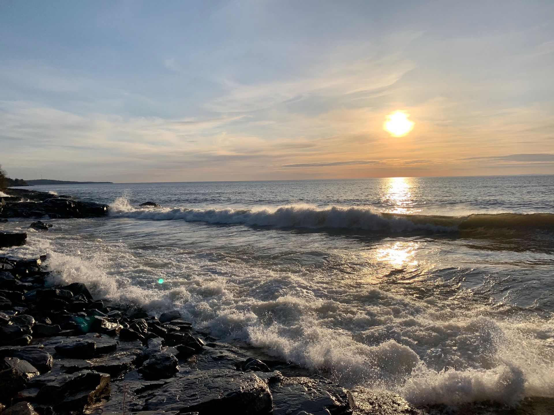 The sun is setting over the ocean and the waves are crashing on the rocks.