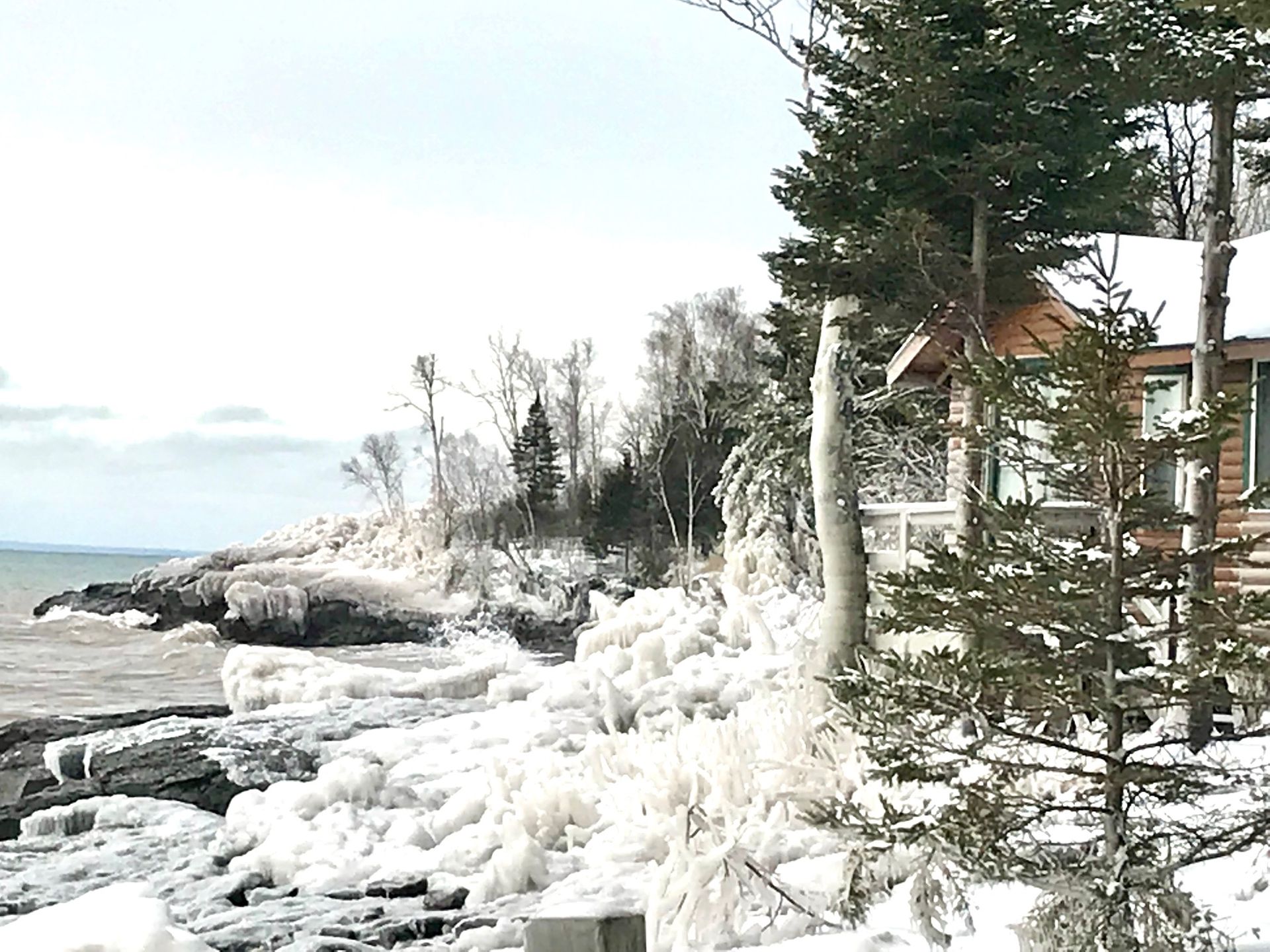 A log cabin sitting on top of a snow covered cliff next to a body of water.