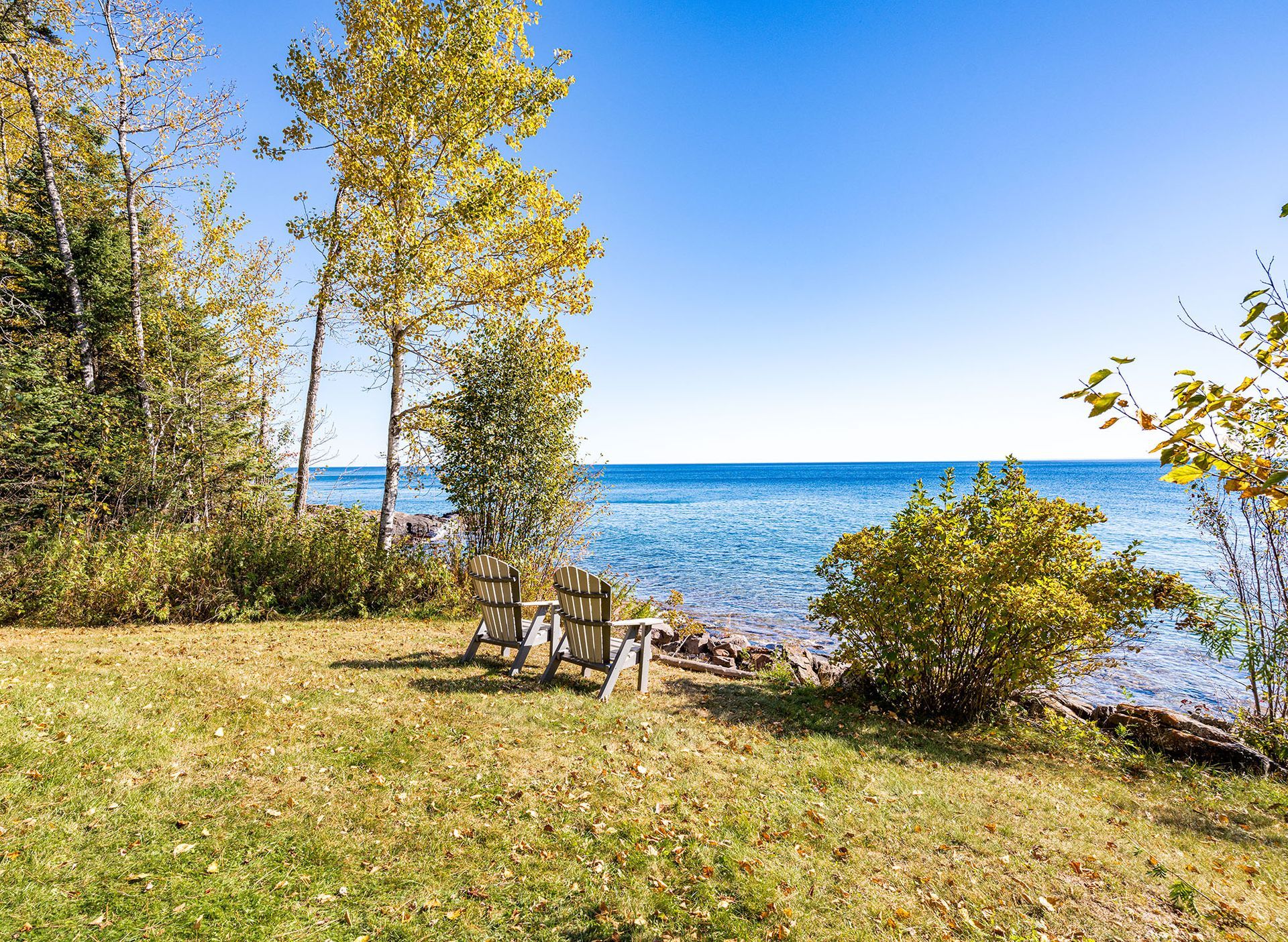 A couple of chairs sitting on top of a lush green field next to a body of water.