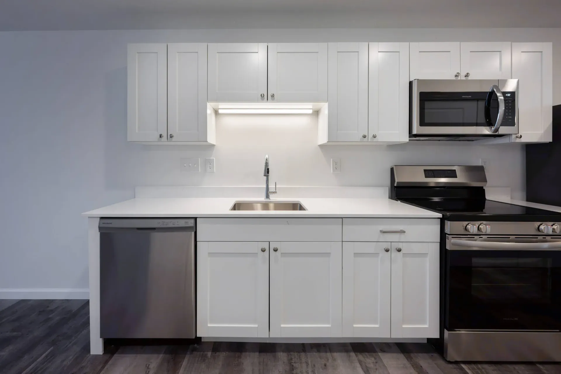 Modern apartment kitchen with white cabinets, stainless sink, dishwasher, microwave, and stove.