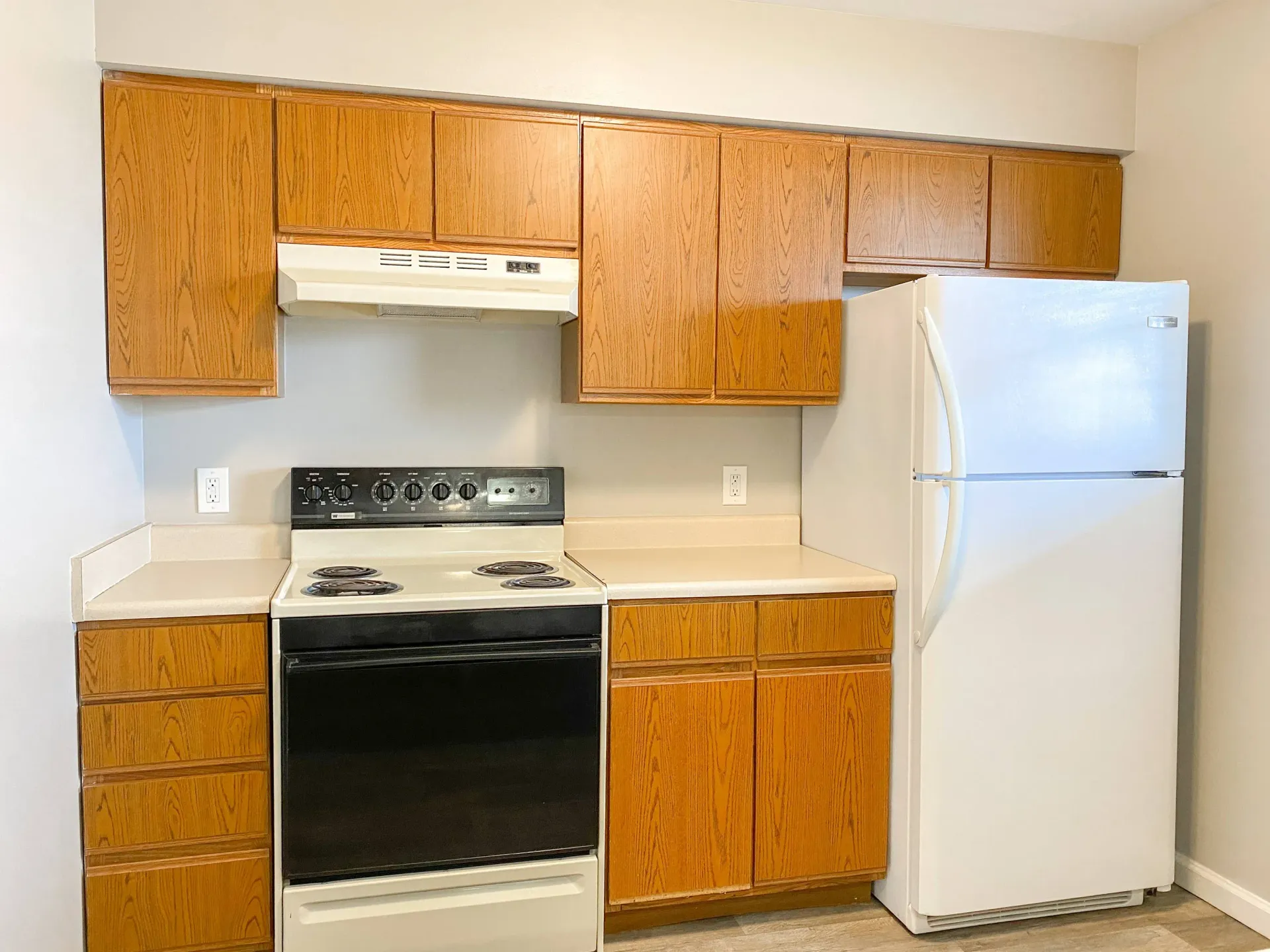 Kitchen in an apartment with wooden cabinets, white refrigerator, and electric stove.