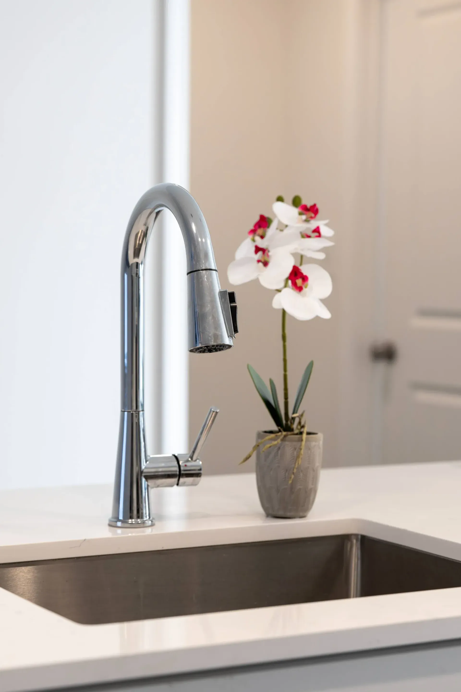 Chrome kitchen faucet over a white countertop with a small potted orchid.