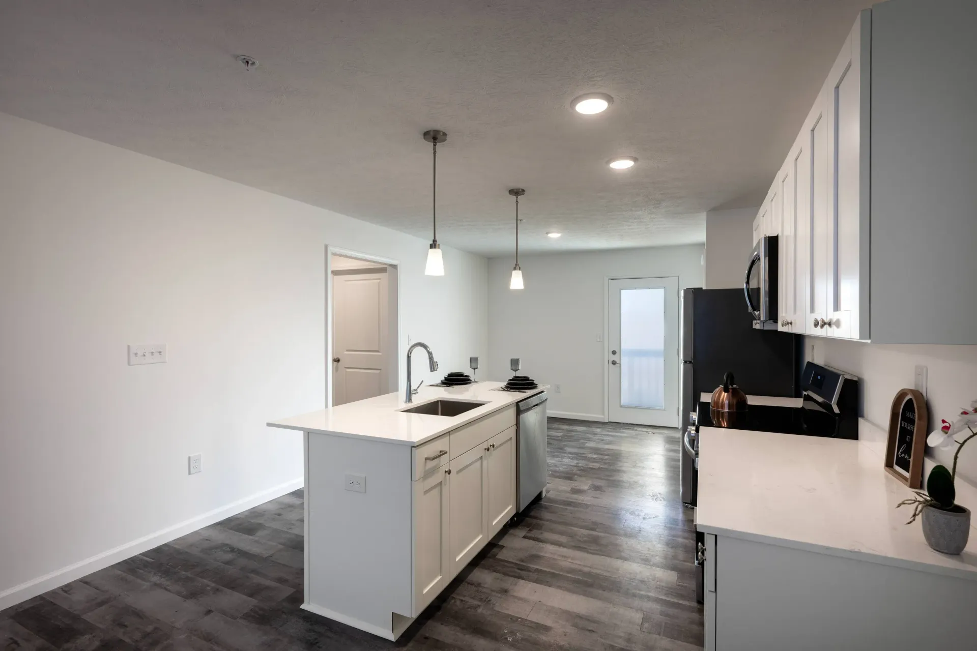 Open-concept apartment kitchen with white cabinets, island sink, pendant lights, and stainless appliances.