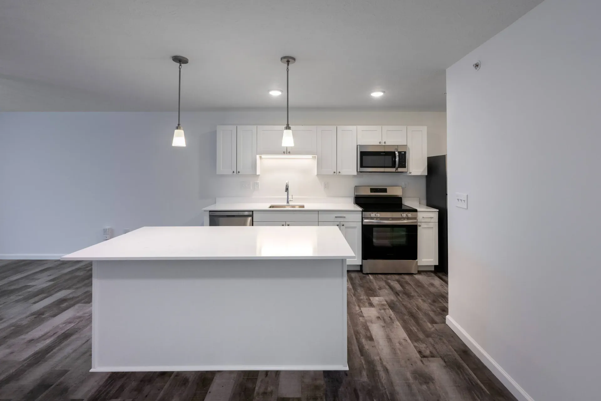 Modern white kitchen with island, white cabinets, stainless steel appliances, and pendant lights.