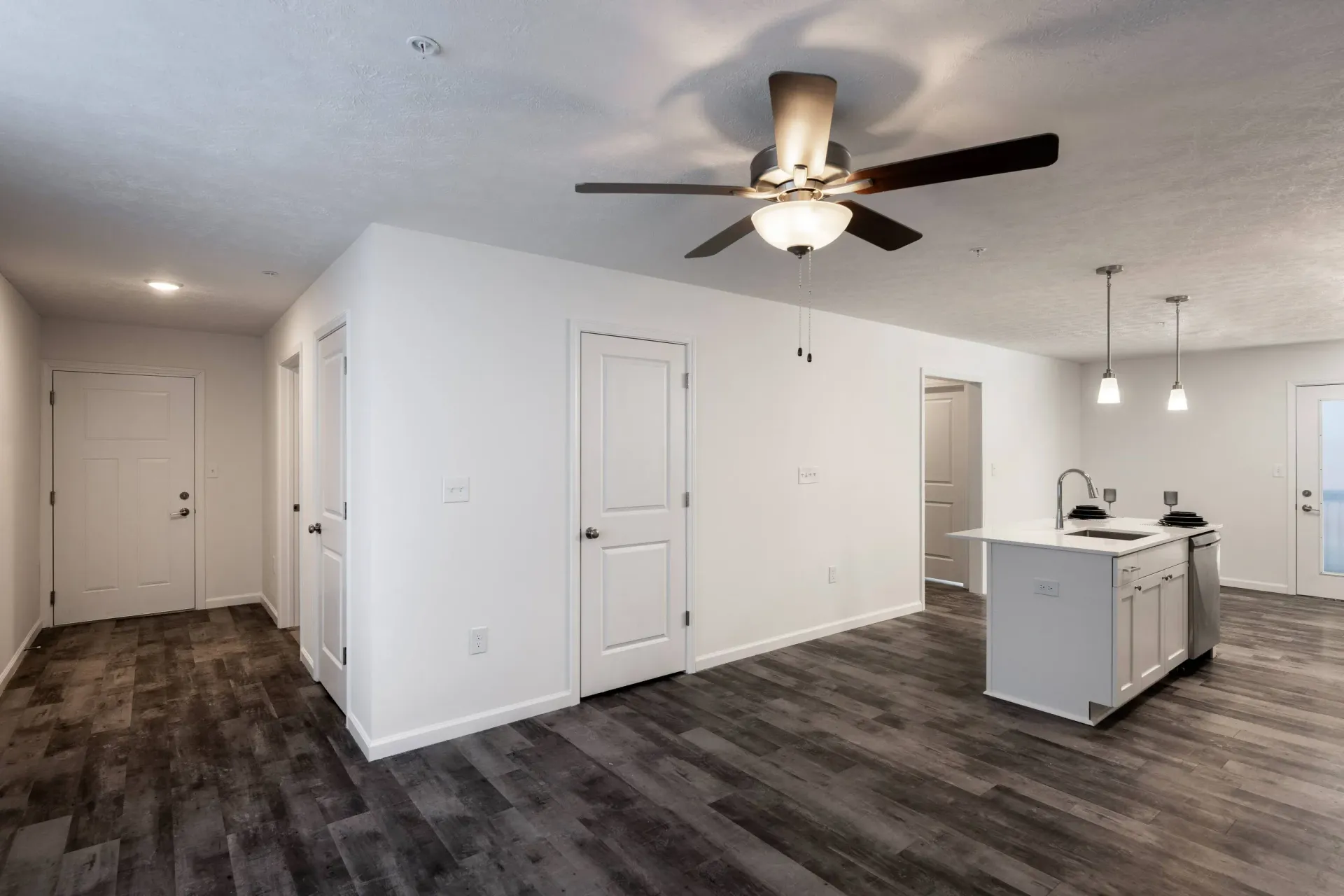 Open-concept apartment living area with kitchen island, white cabinetry, and dark wood-look flooring.