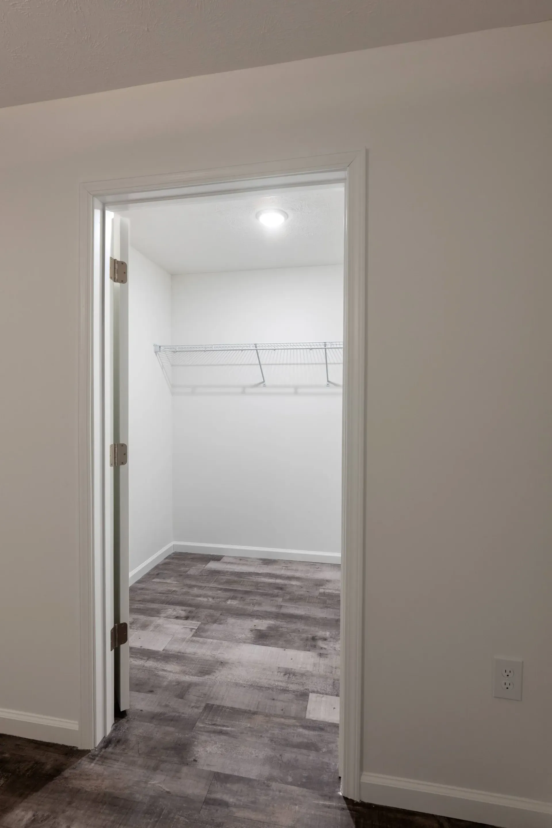 Walk-in closet with a white wire shelf, bright ceiling light, and wood-look flooring.