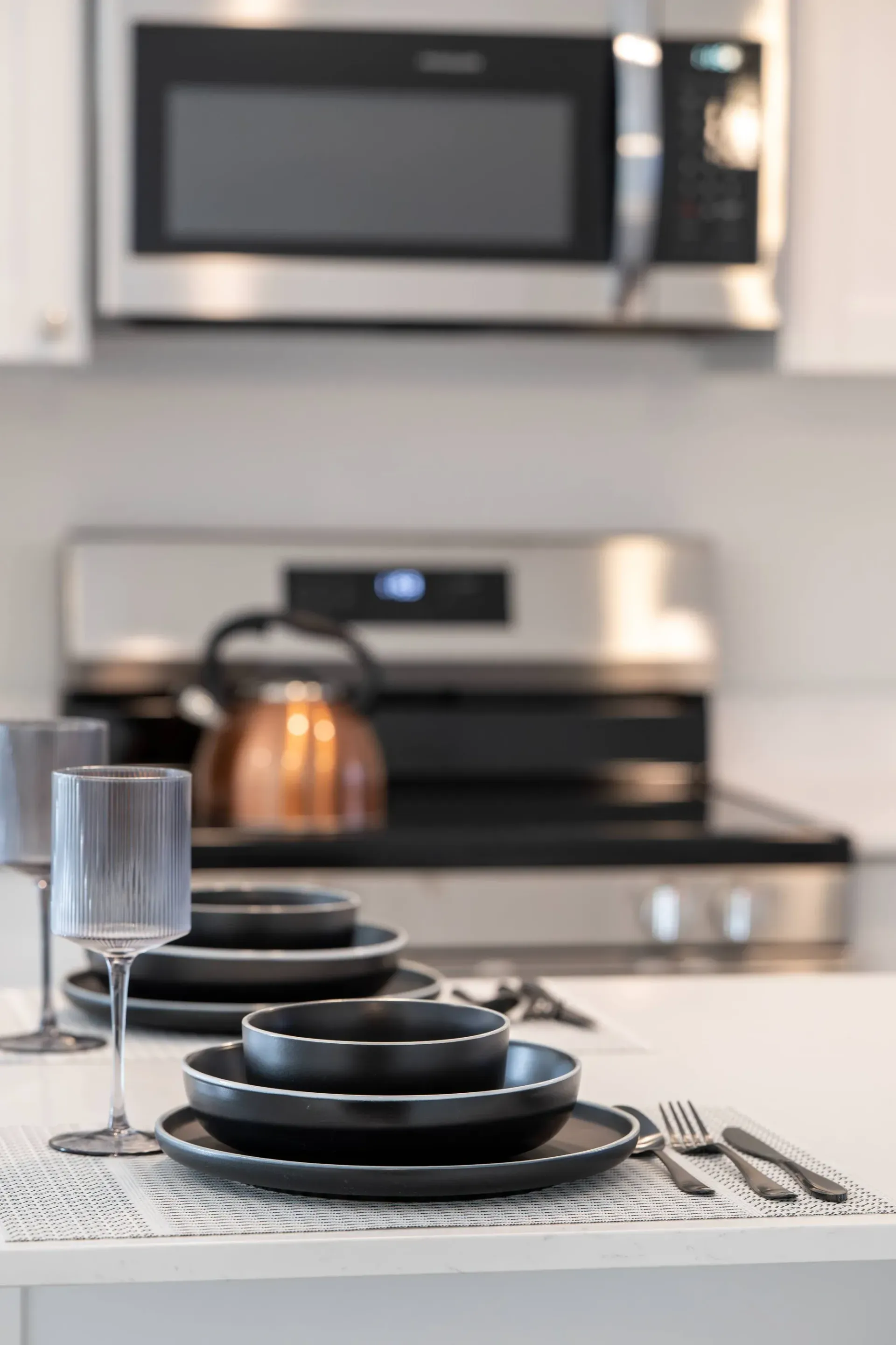 Modern kitchen with black dishware on a white counter and stainless-steel appliances.