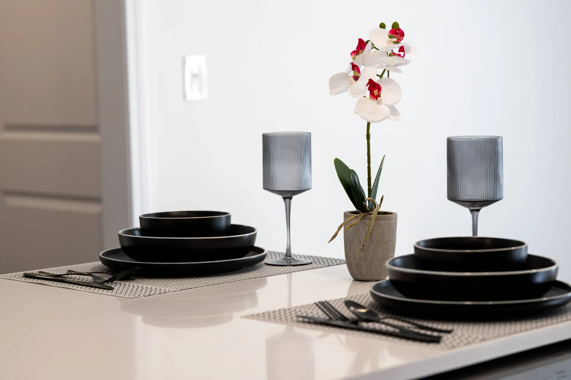 Dining table with black plates, gray ribbed goblets, and a potted orchid centerpiece.