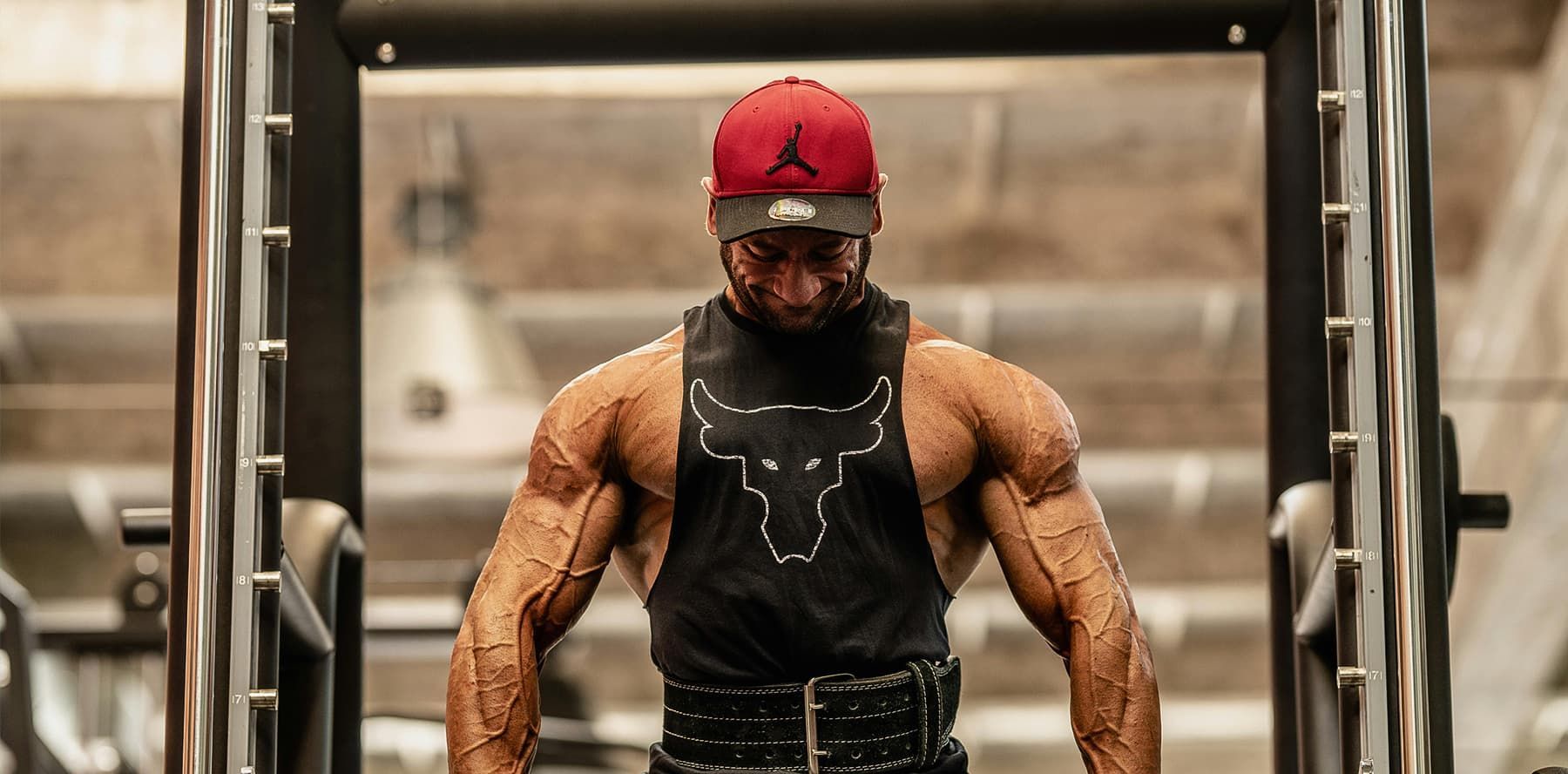 A man wearing a red hat and a black tank top is standing in a gym.