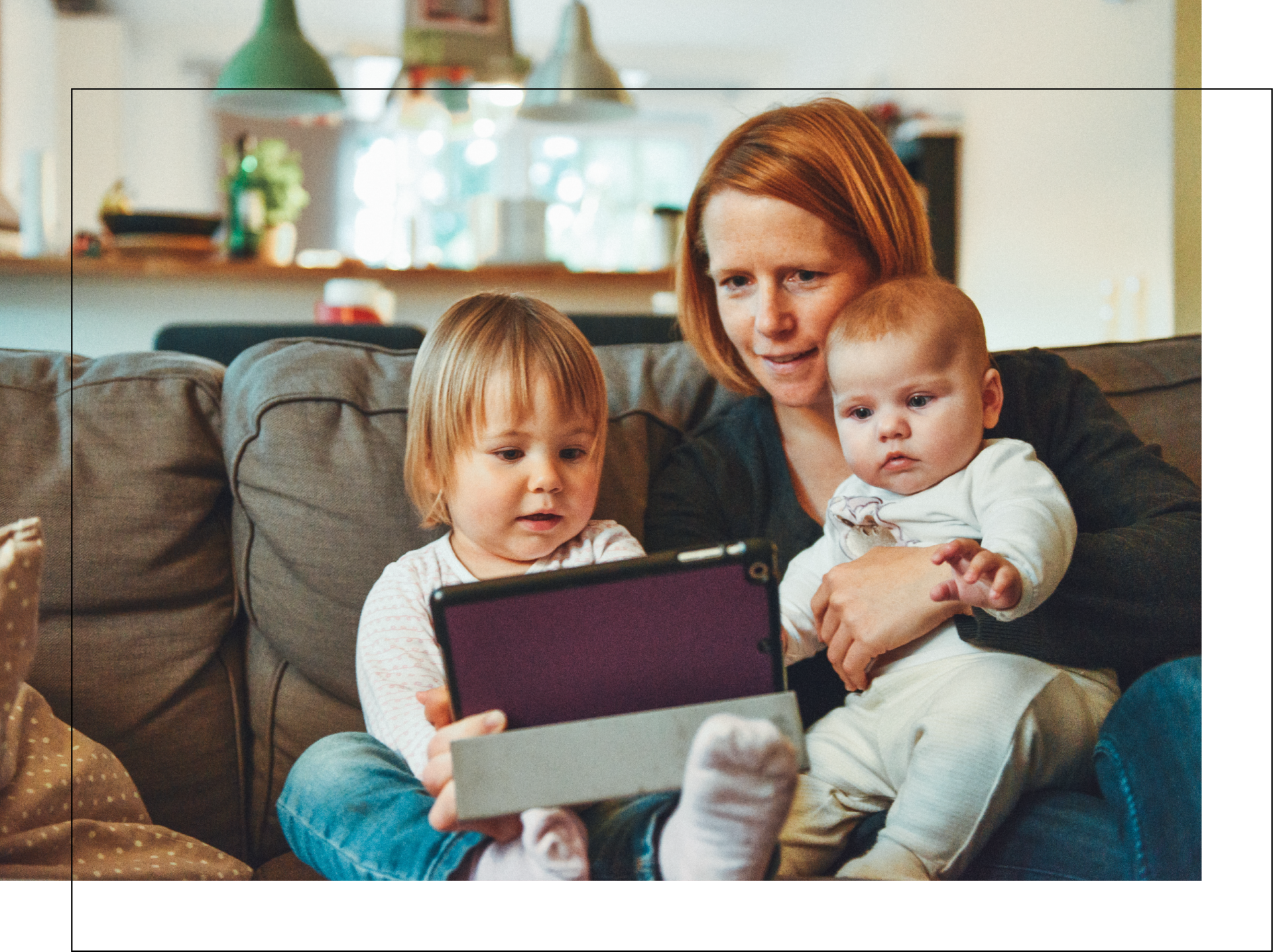 A woman and two children are sitting on a couch looking at a tablet.