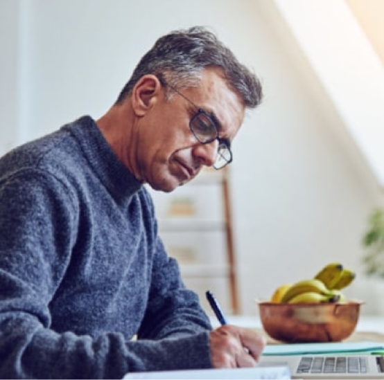 A man wearing glasses is writing on a piece of paper