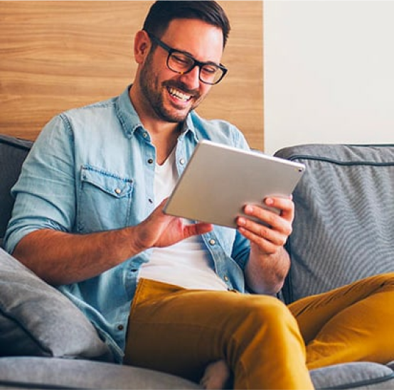 A man is sitting on a couch using a tablet computer.