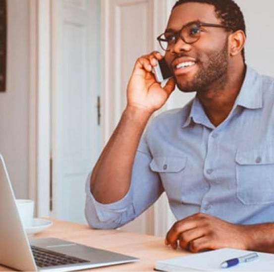 A man is sitting at a desk talking on a cell phone
