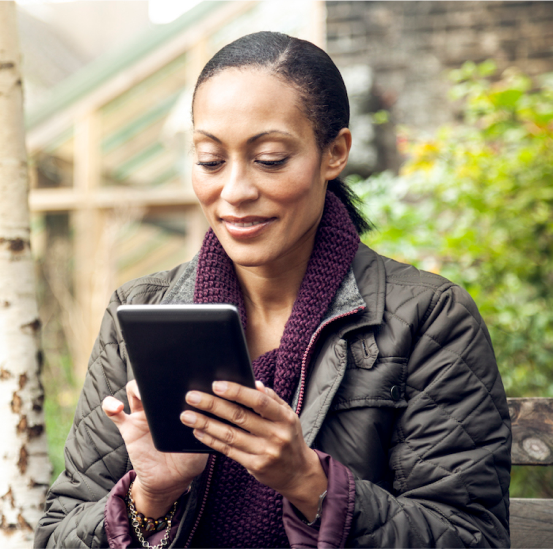 A woman is sitting on a bench looking at her tablet