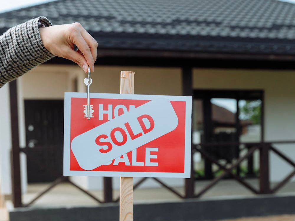 A person is holding a sold sign in front of a house.