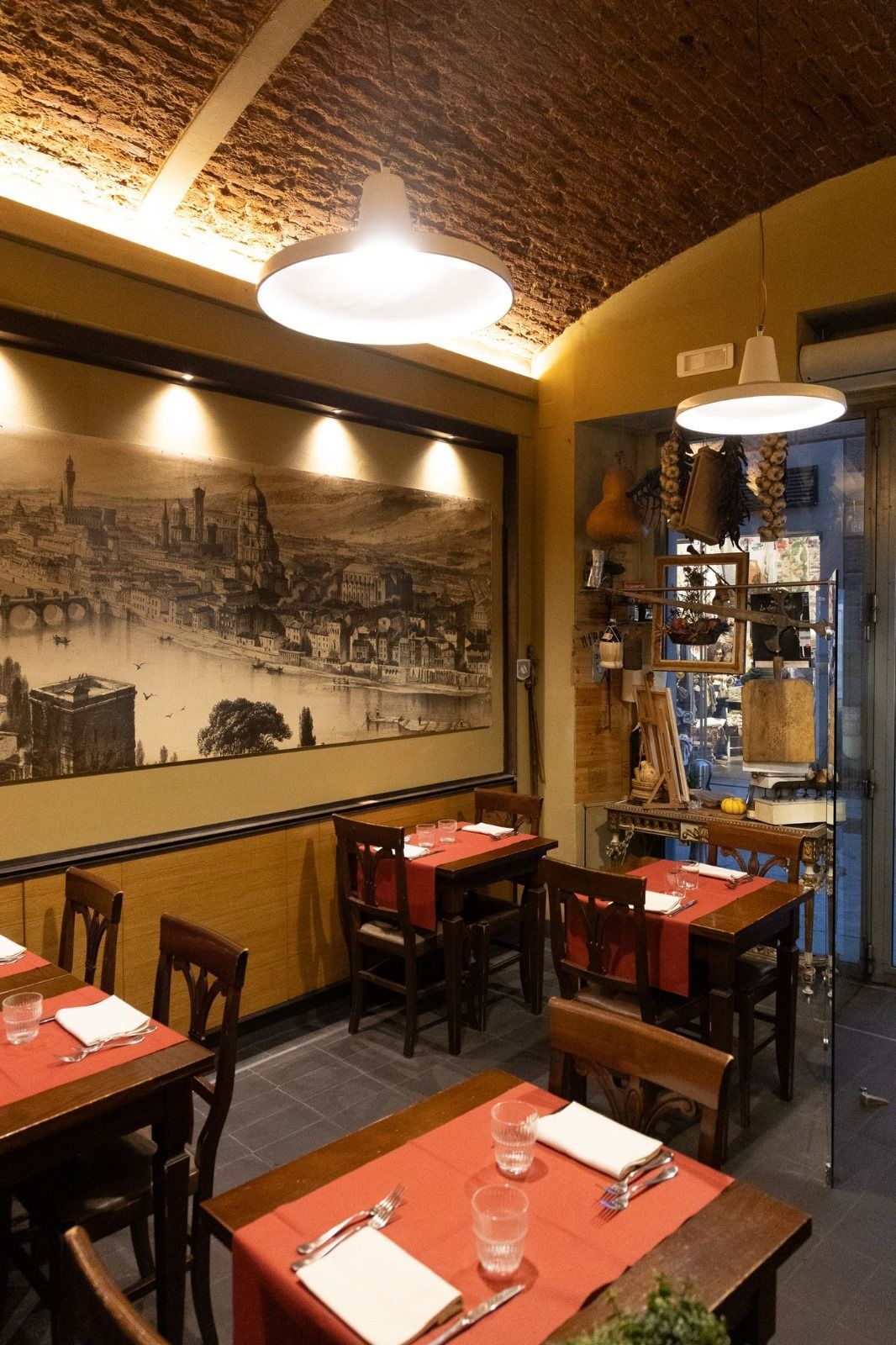 Interno del ristorante con tavoli apparecchiati di rosso, mobili in legno scuro e un grande murale raffigurante la città.