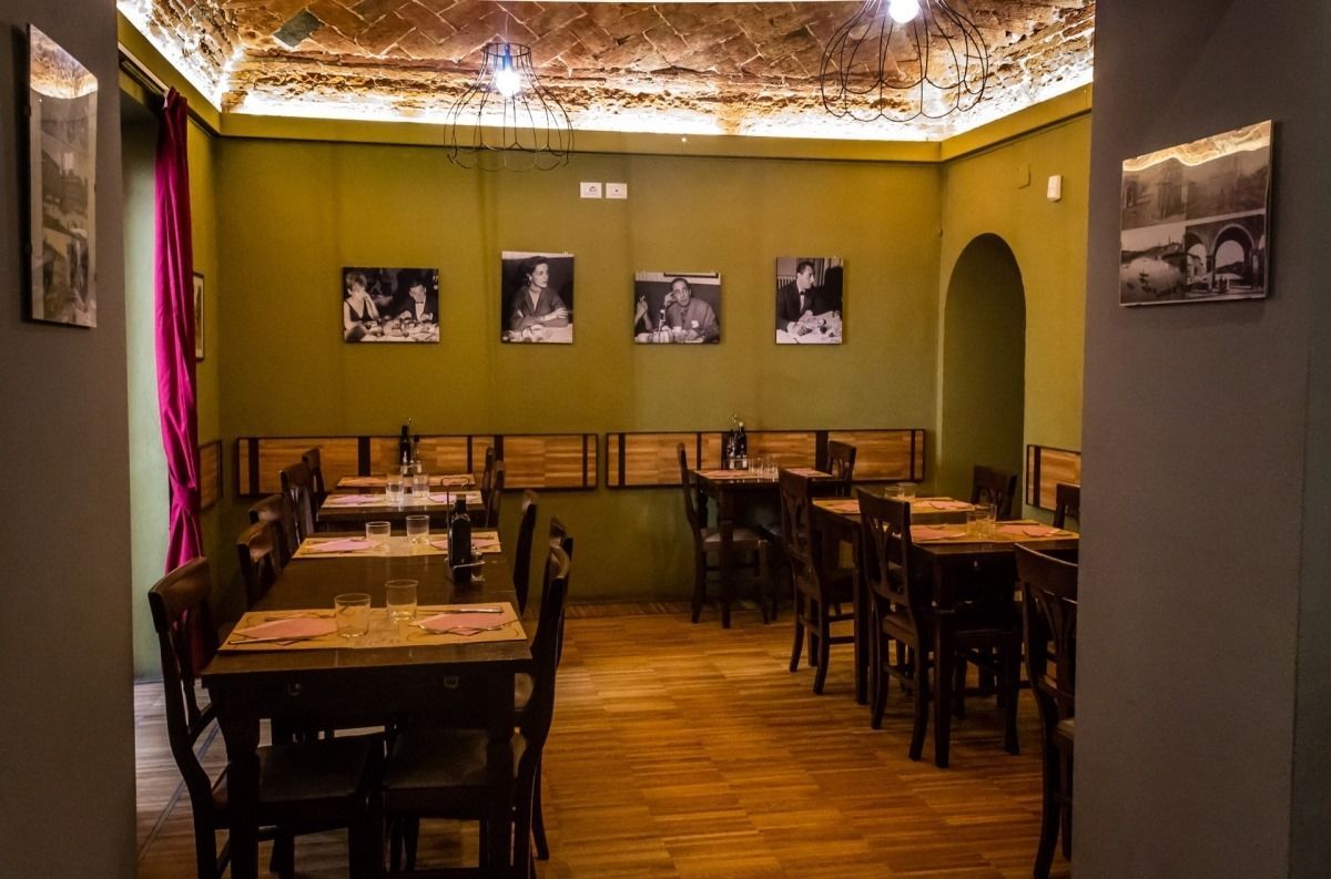 Interno vuoto del ristorante, pareti verde oliva, tavoli e sedie in legno, porta ad arco.