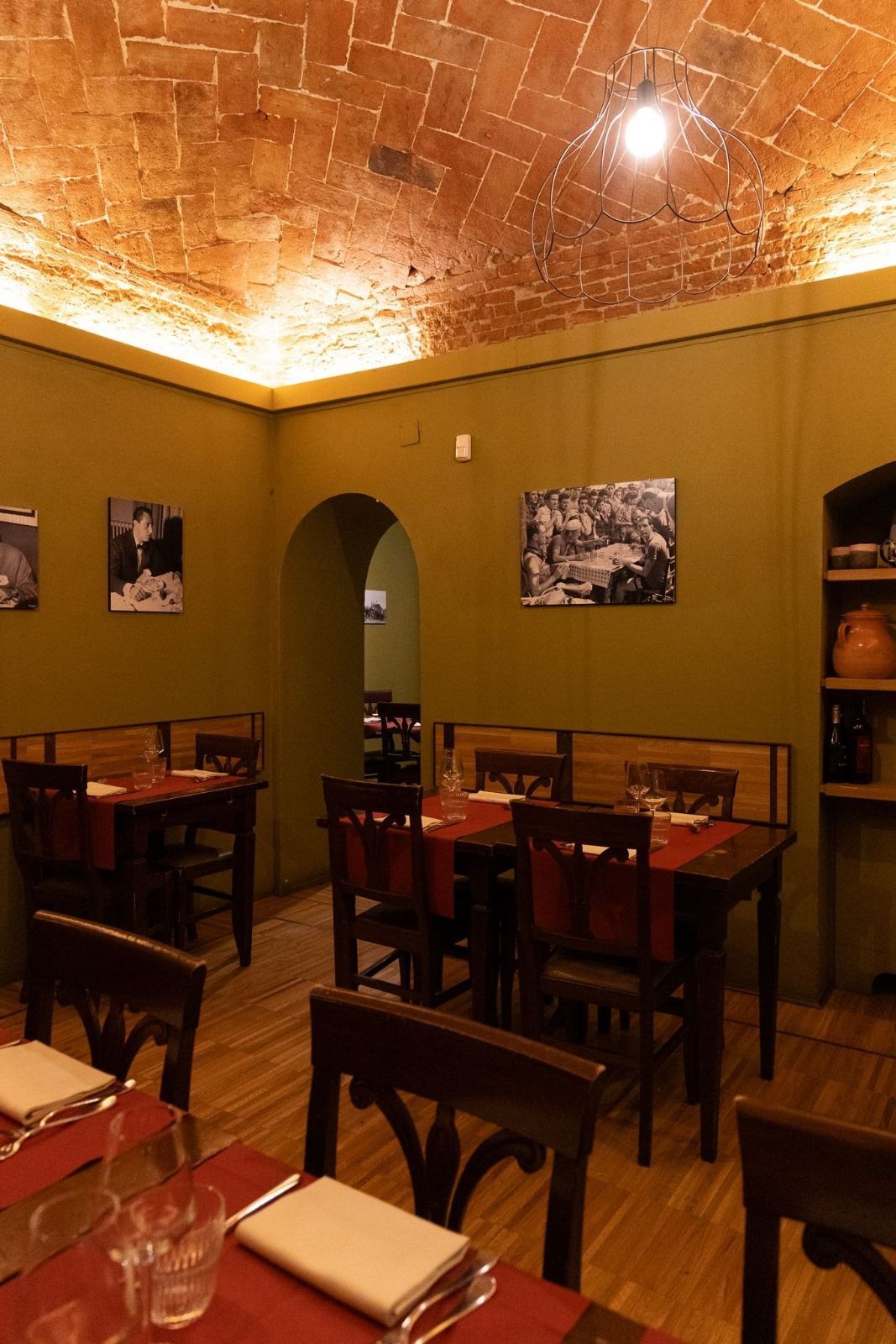 Interno di un ristorante con tavoli in legno, tovagliette rosse e soffitto in mattoni.