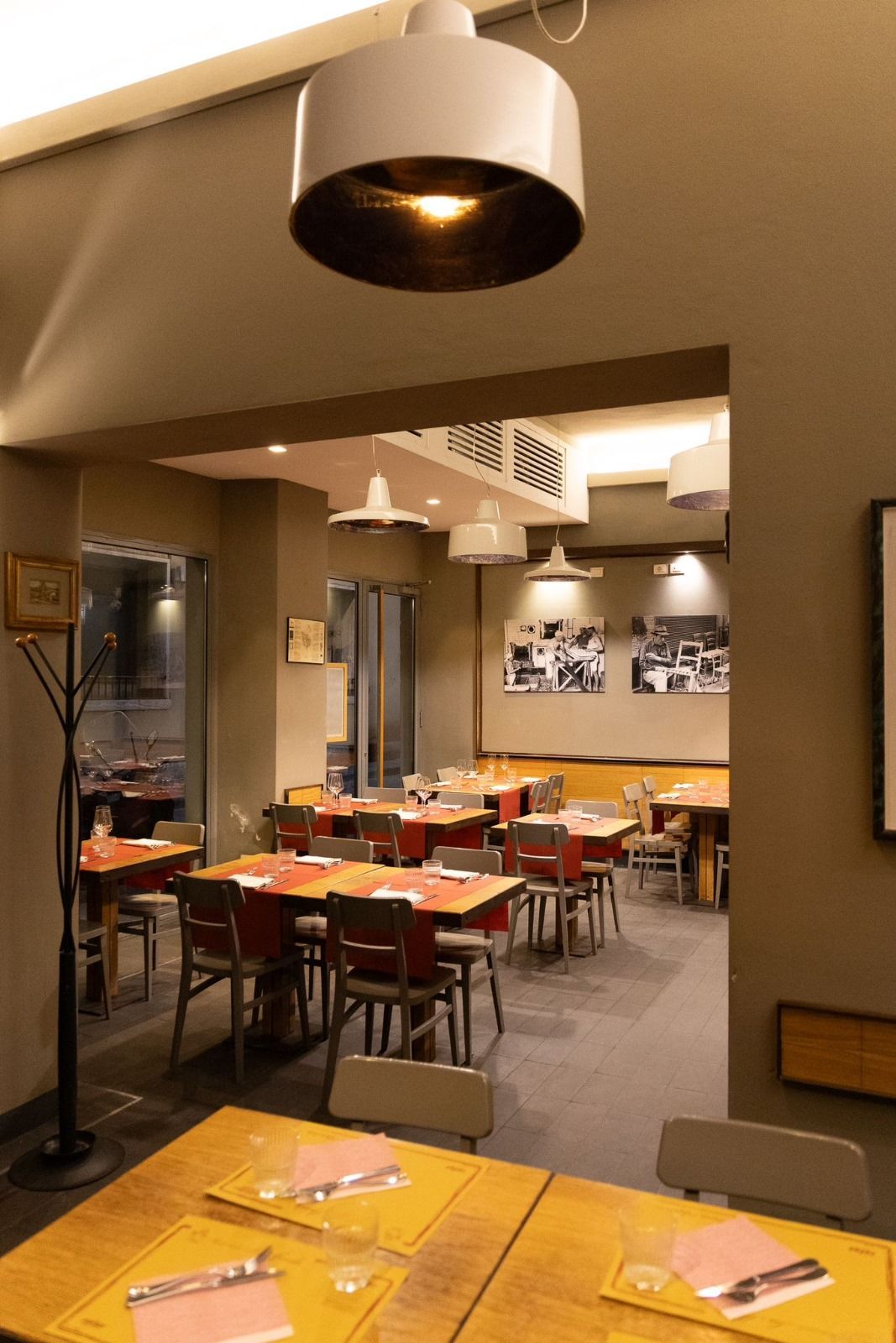 Interno del ristorante con tavoli, sedie e illuminazione dall'alto. Pareti grigie, toni caldi e un'atmosfera accogliente.