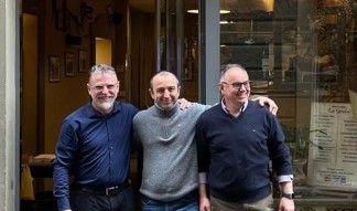 Tre uomini sono in piedi fuori da un edificio, abbracciati, sorridenti.