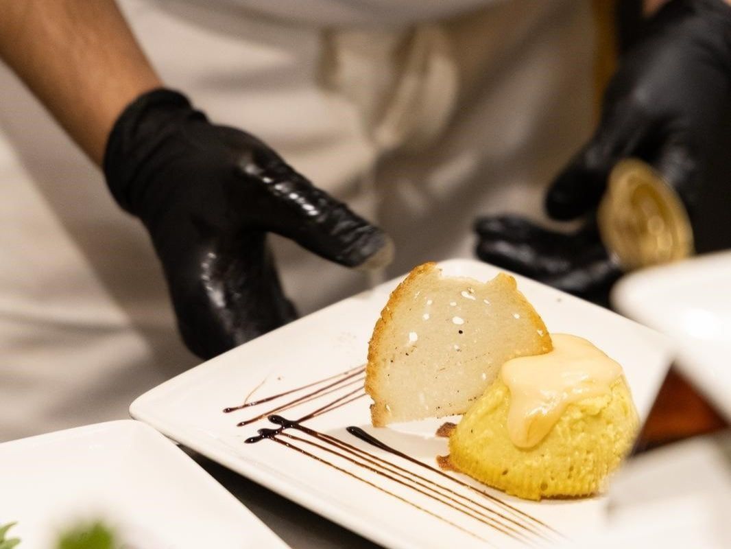 Lo chef con i guanti neri sistema il formaggio e la pasta gialla con la salsa su un piatto bianco.