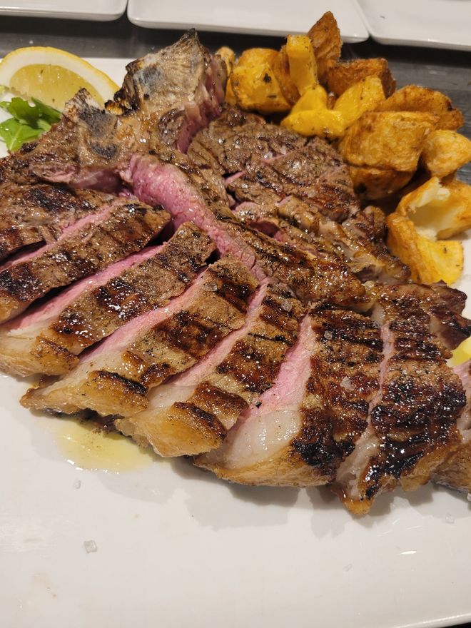 Bistecca alla griglia affettata con patate su un piatto bianco, una fetta di limone a sinistra.
