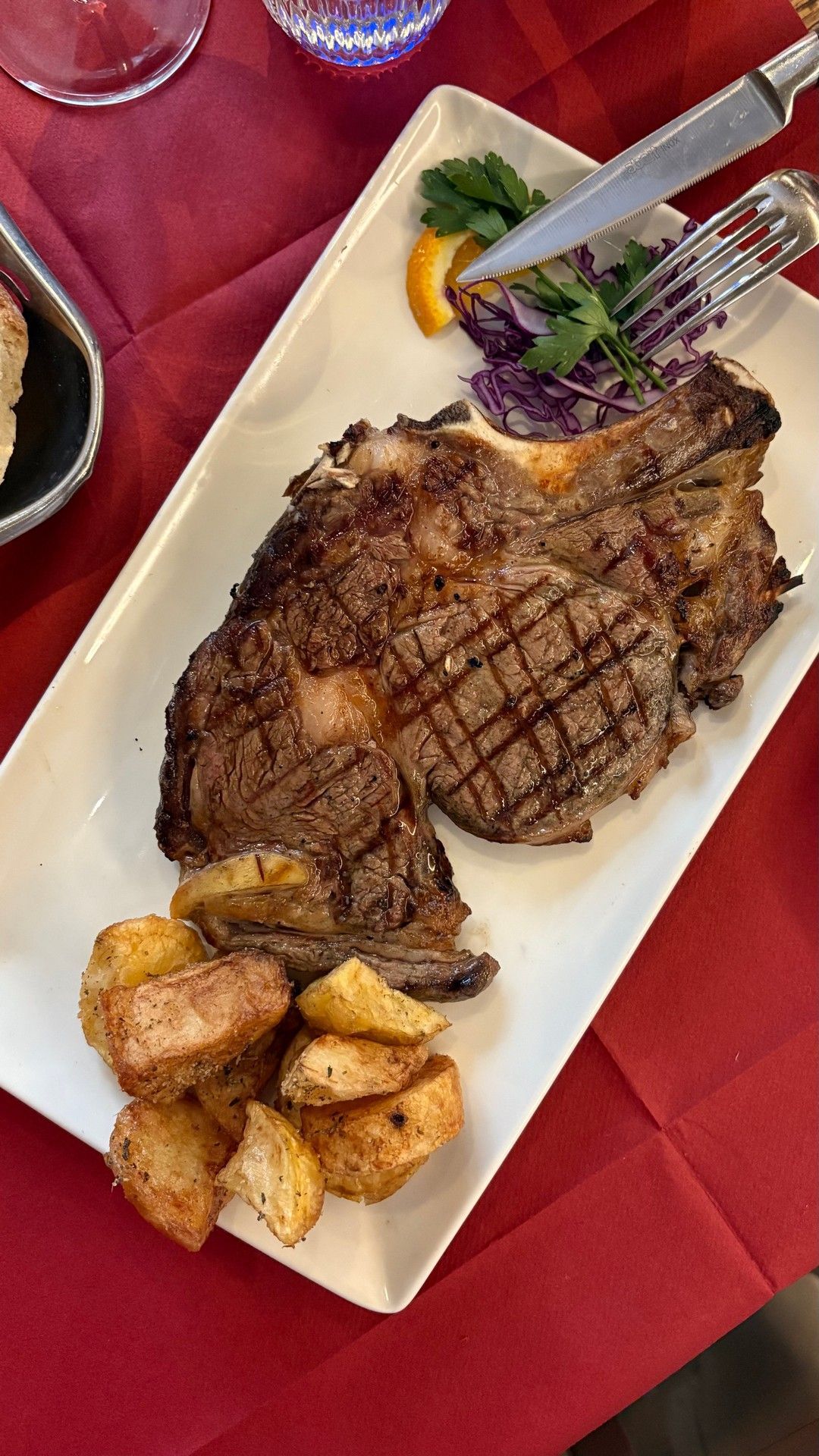 Bistecca alla griglia con patate su un piatto bianco, tovaglia rossa.