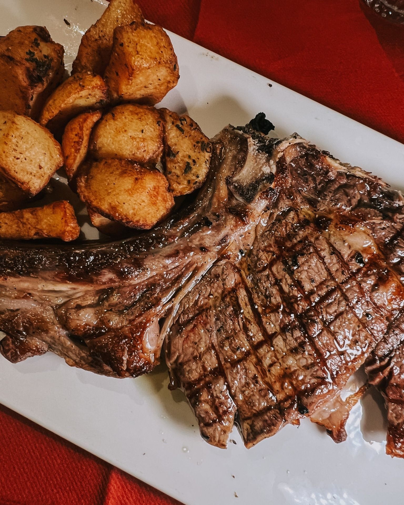 Bistecca alla griglia e patate su un piatto bianco; tonalità marroni e dorate.