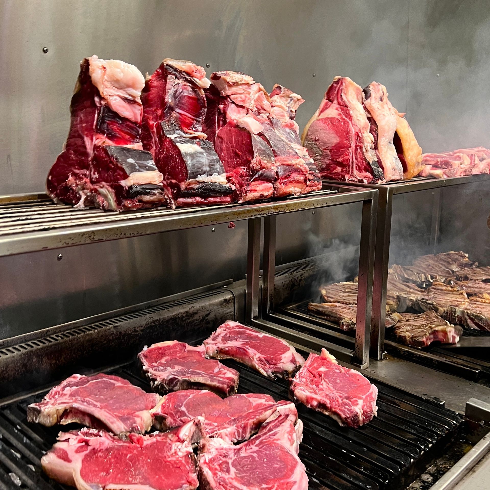 Bistecche di manzo crude su griglie e grigliate su una griglia metallica in cucina.