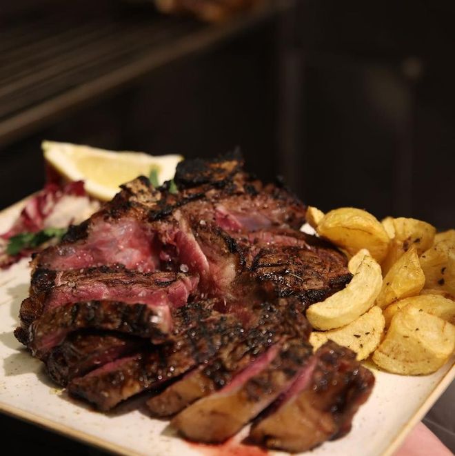 Bistecca alla griglia con pezzi tagliati a fette, spicchi di patate, spicchio di limone e verdure su un piatto.
