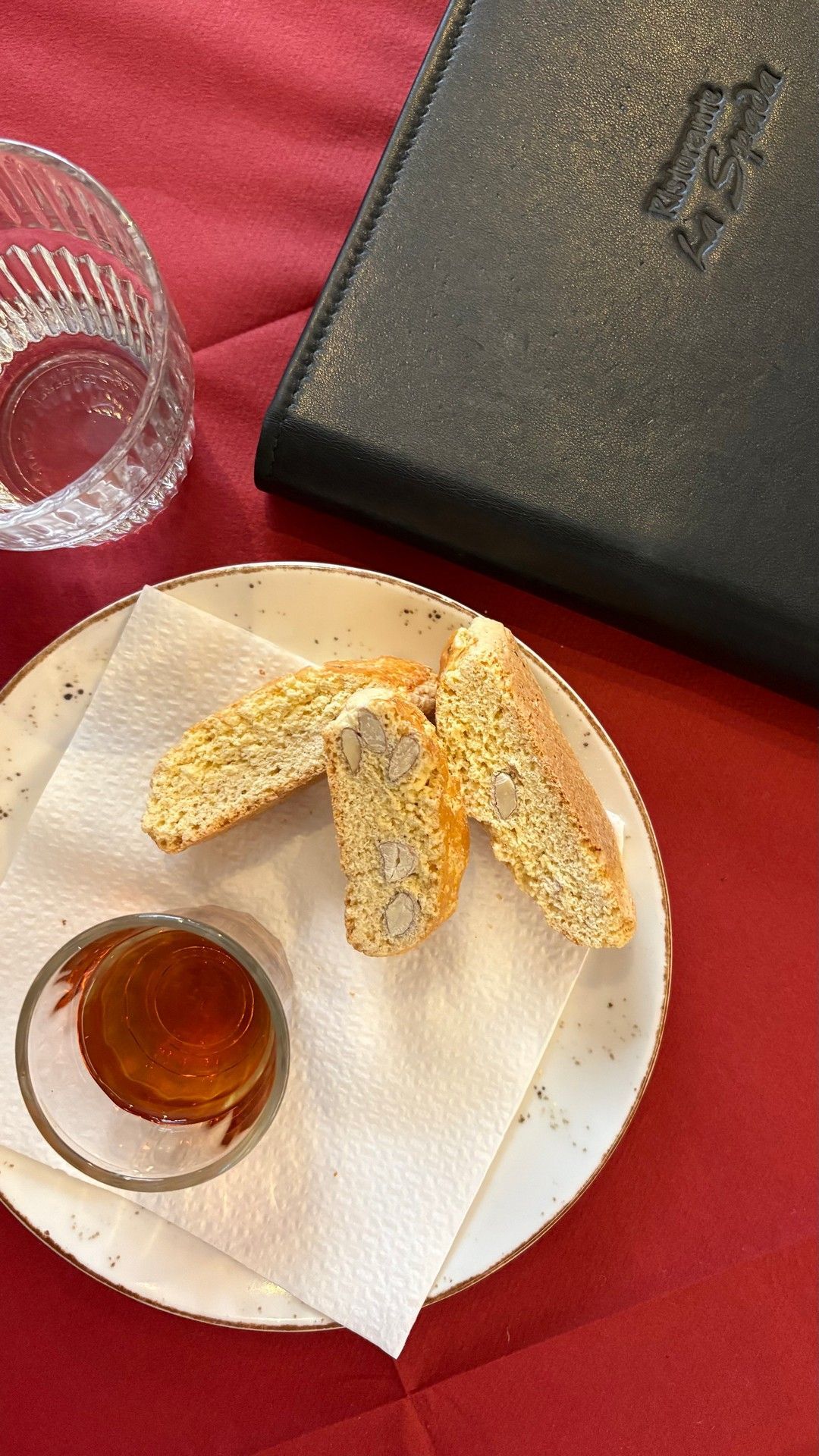 Piatto con biscotti e miele, su una tovaglia rossa accanto a un bicchiere e al menu.
