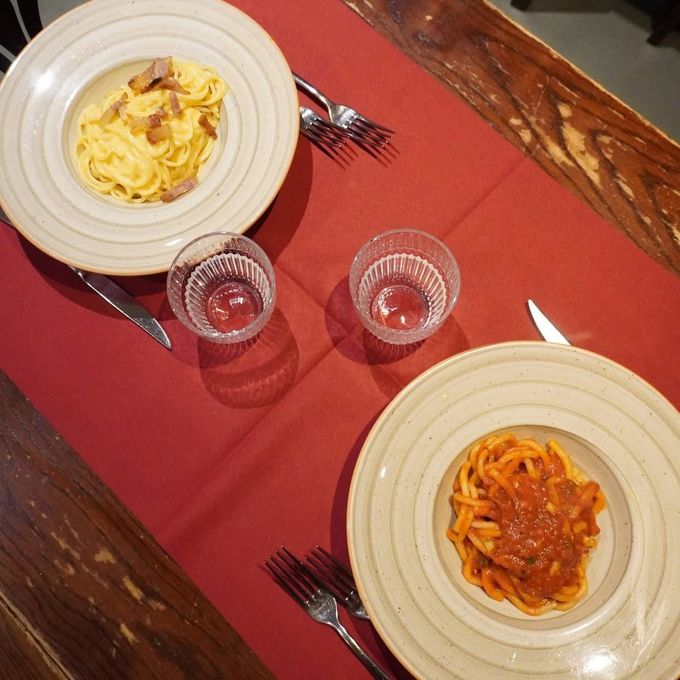 Due piatti di pasta, bicchieri e posate su una tovaglia rossa, tavolo di legno.