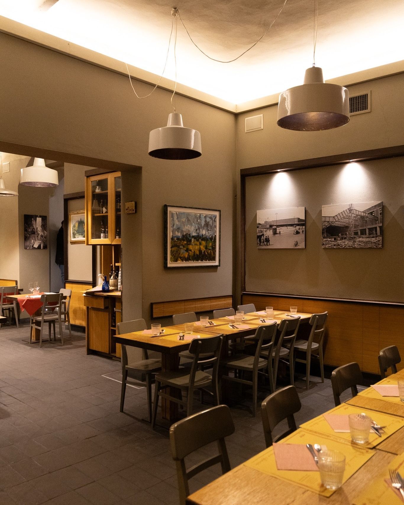 Interno del ristorante con tavoli, sedie e luci a soffitto. Sono visibili anche opere d'arte e una vetrina.