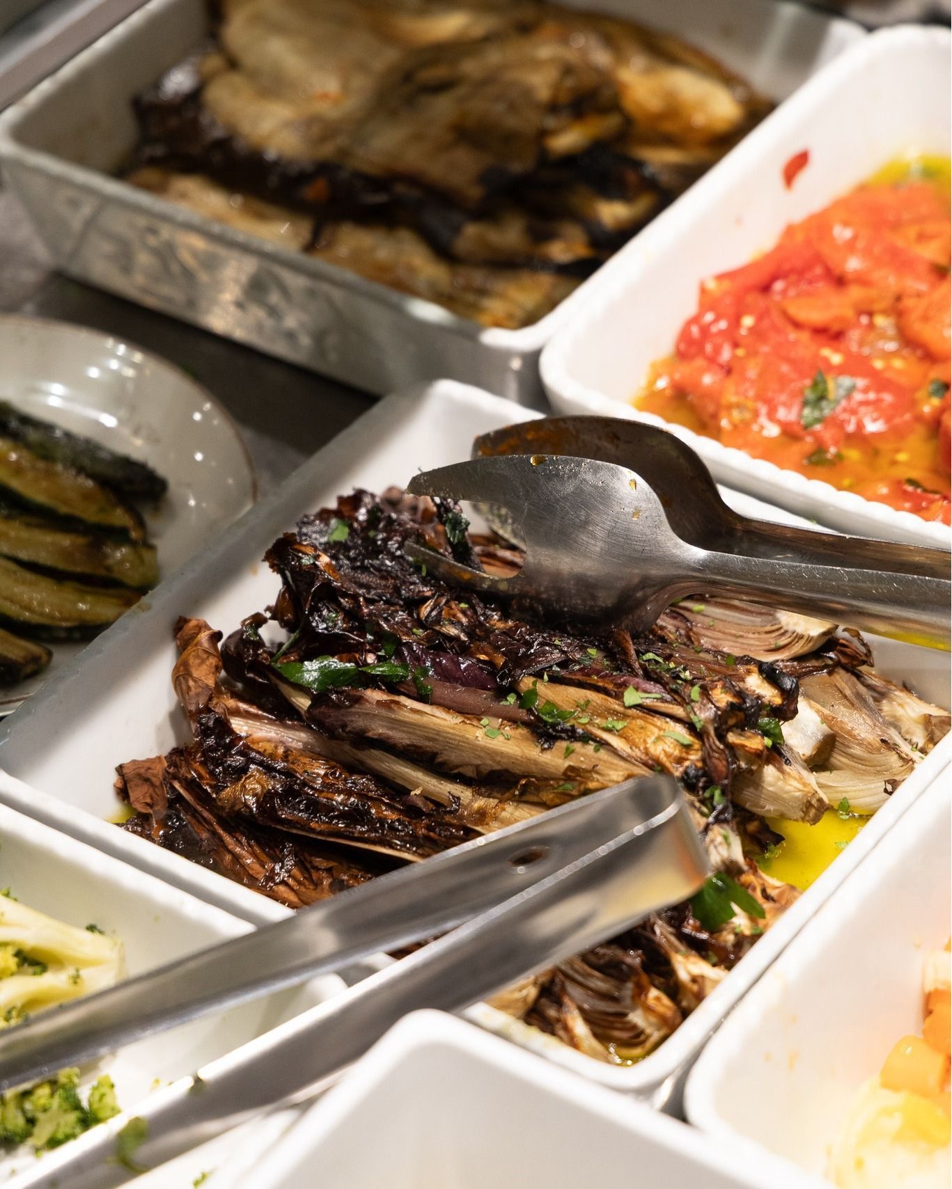 Insalate con verdure arrostite: melanzane, pomodori, zucchine e radicchio, con pinze da portata.