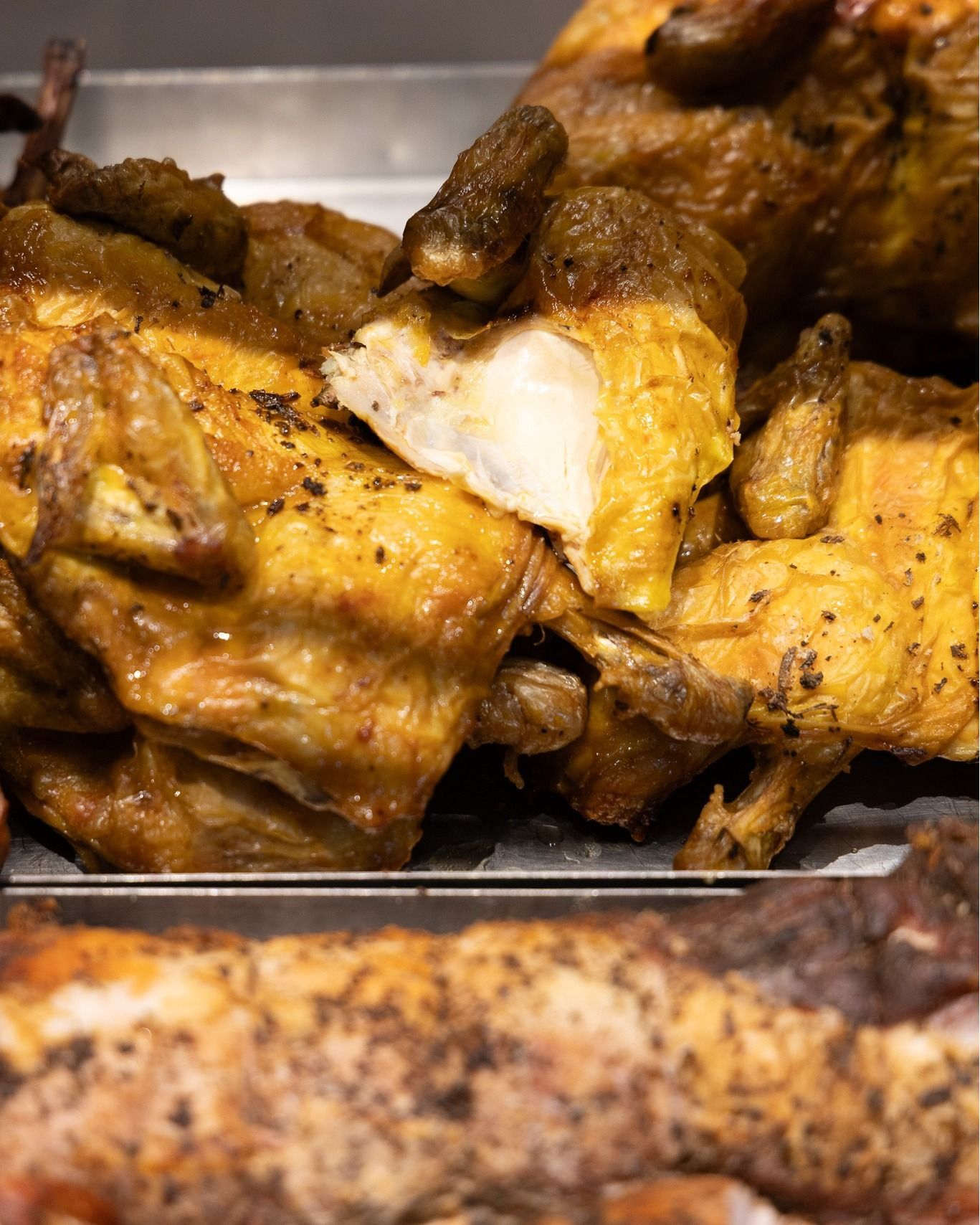 Pezzi di pollo arrosto esposti in un contenitore, pelle dorata, un pezzo tagliato parzialmente.