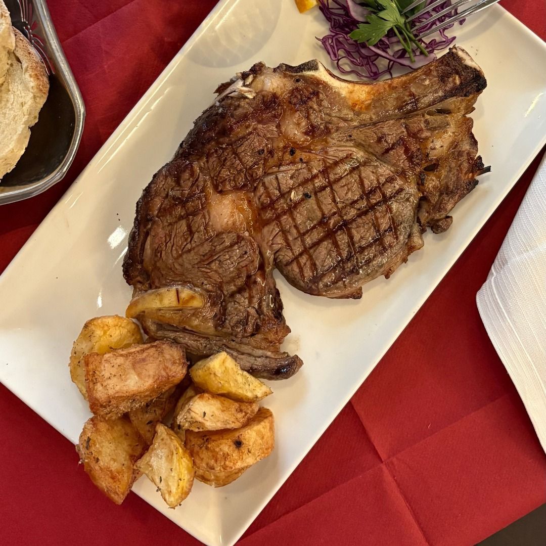 Bistecca alla griglia con patate e insalata su un piatto bianco, tovaglia rossa.