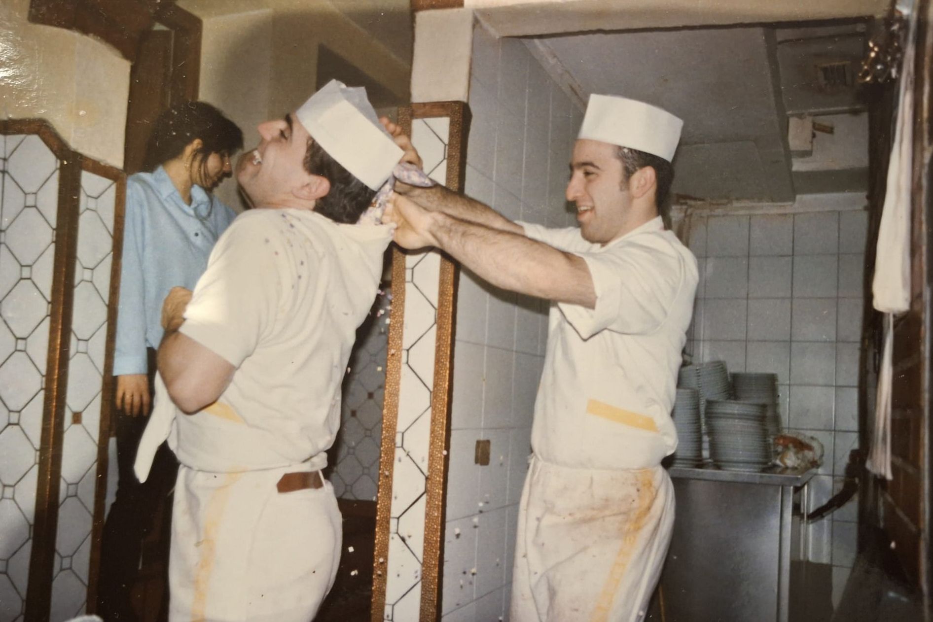 Due cuochi in uniforme bianca si rovesciano scherzosamente qualcosa sulla testa in cucina.