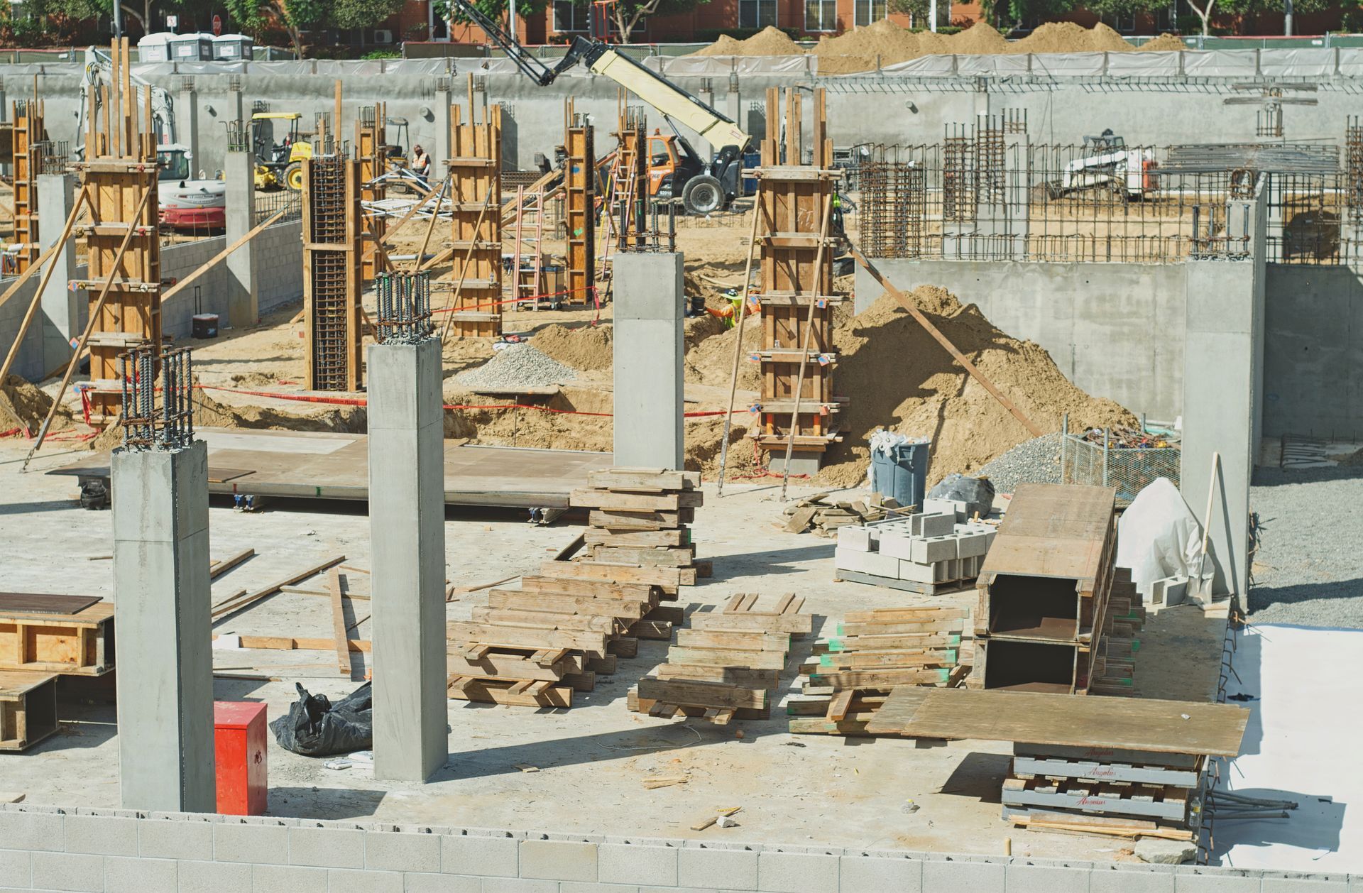 Chantier de construction avec colonnes en béton, coffrages en bois et matériaux de construction.