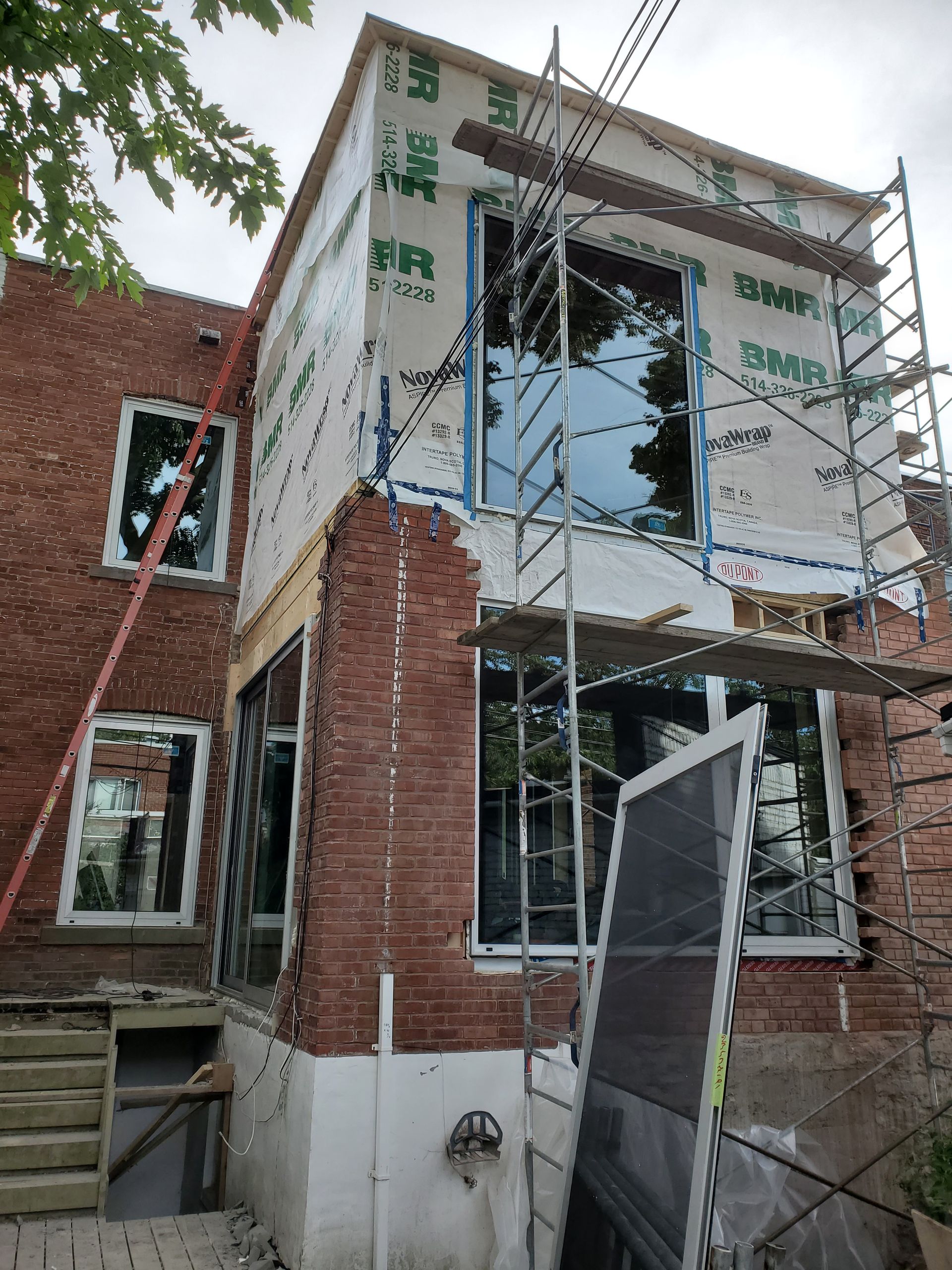 Un bâtiment en briques est en cours de rénovation avec des échafaudages et une porte moustiquaire.