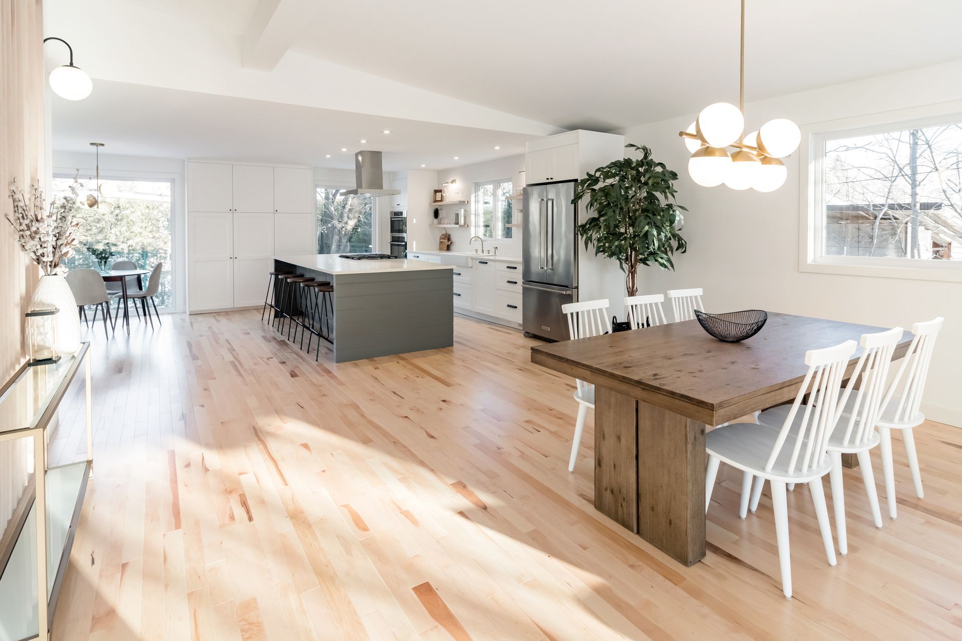 Une salle à manger avec une table et des chaises en bois et une cuisine en arrière-plan.