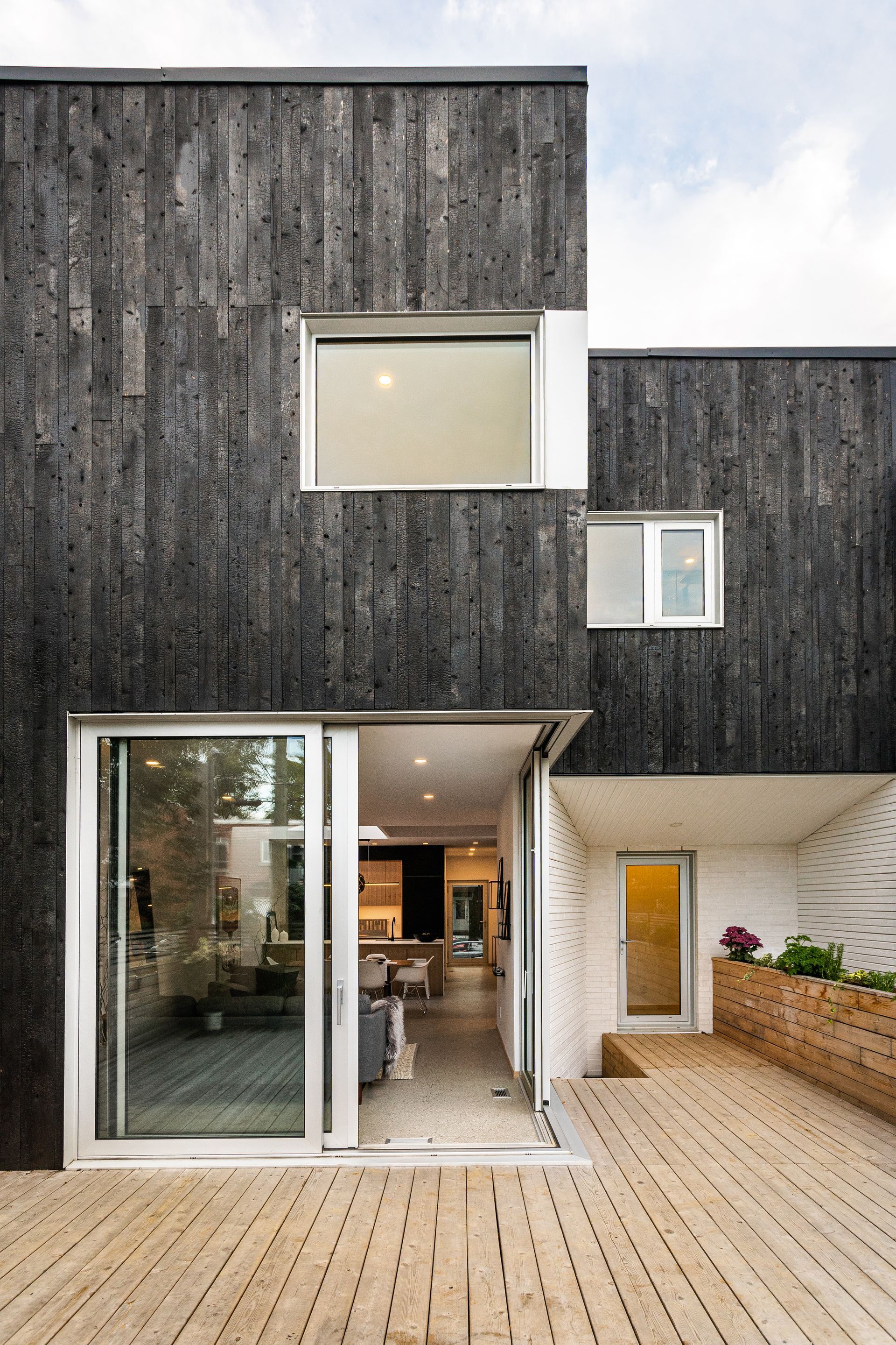 Une maison noire et blanche avec une porte coulissante en verre et une terrasse en bois.