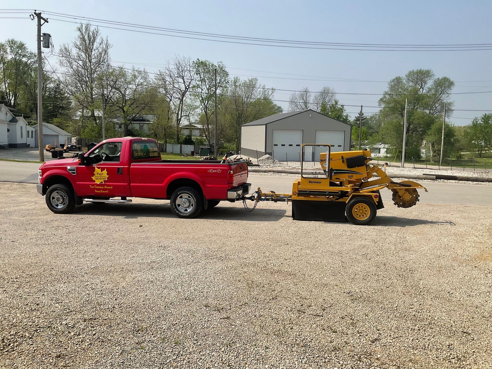 A red truck is towing a yellow tractor on a trailer.