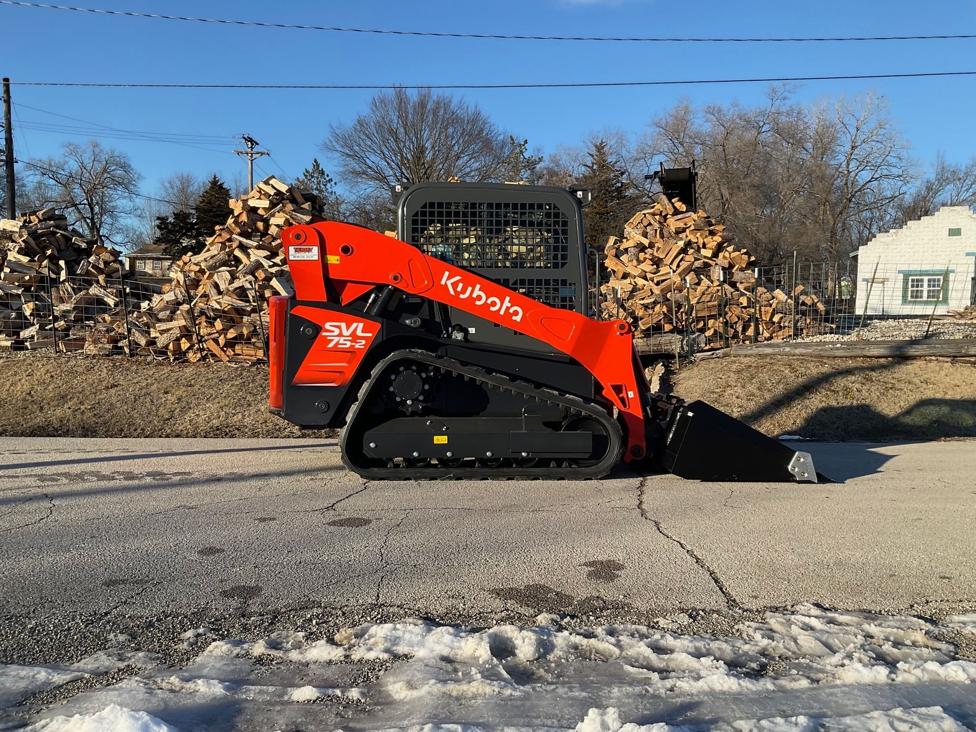 A red skid steer is parked on the side of the road next to a pile of logs.