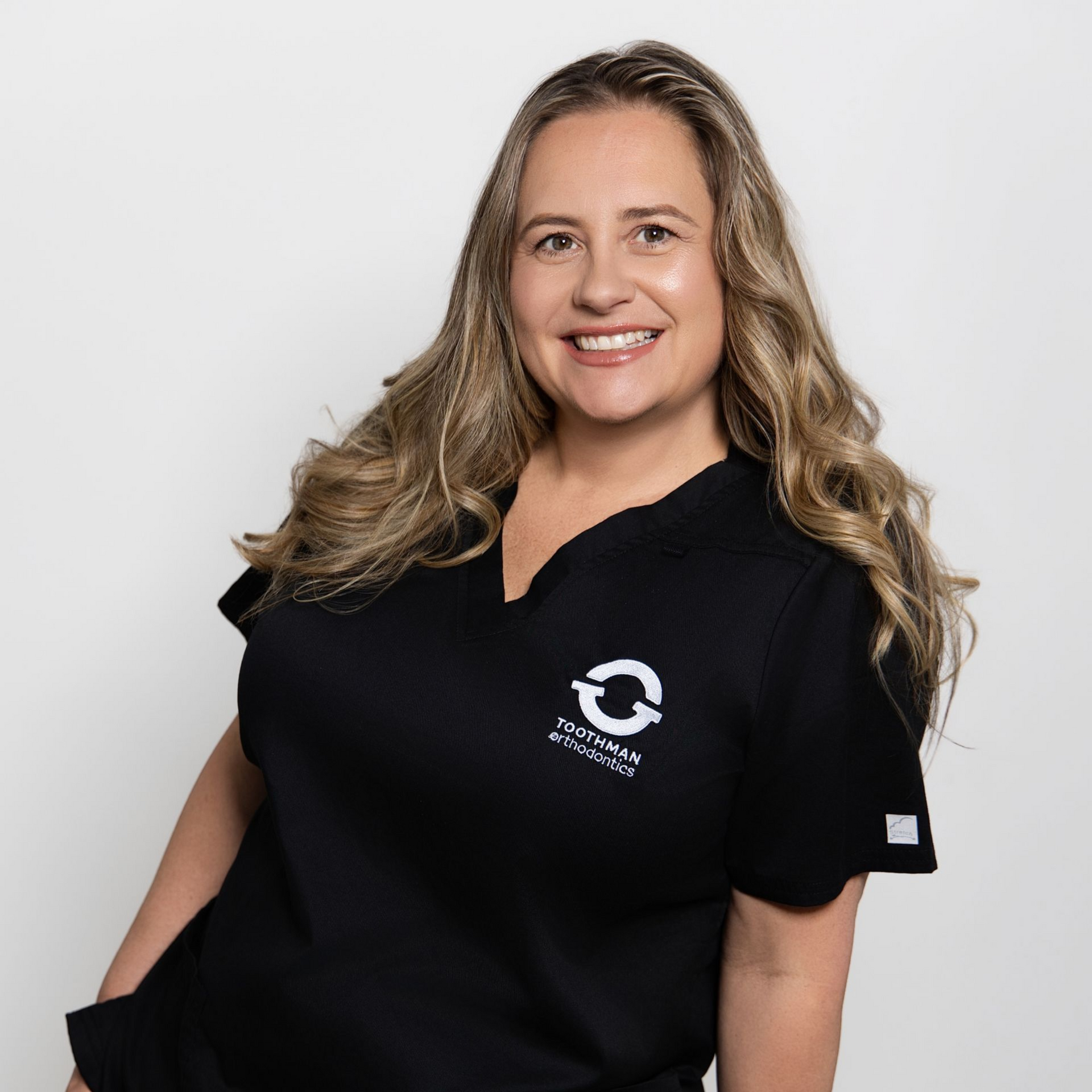 Smiling woman in black polo shirt with logo, standing against a light gray background